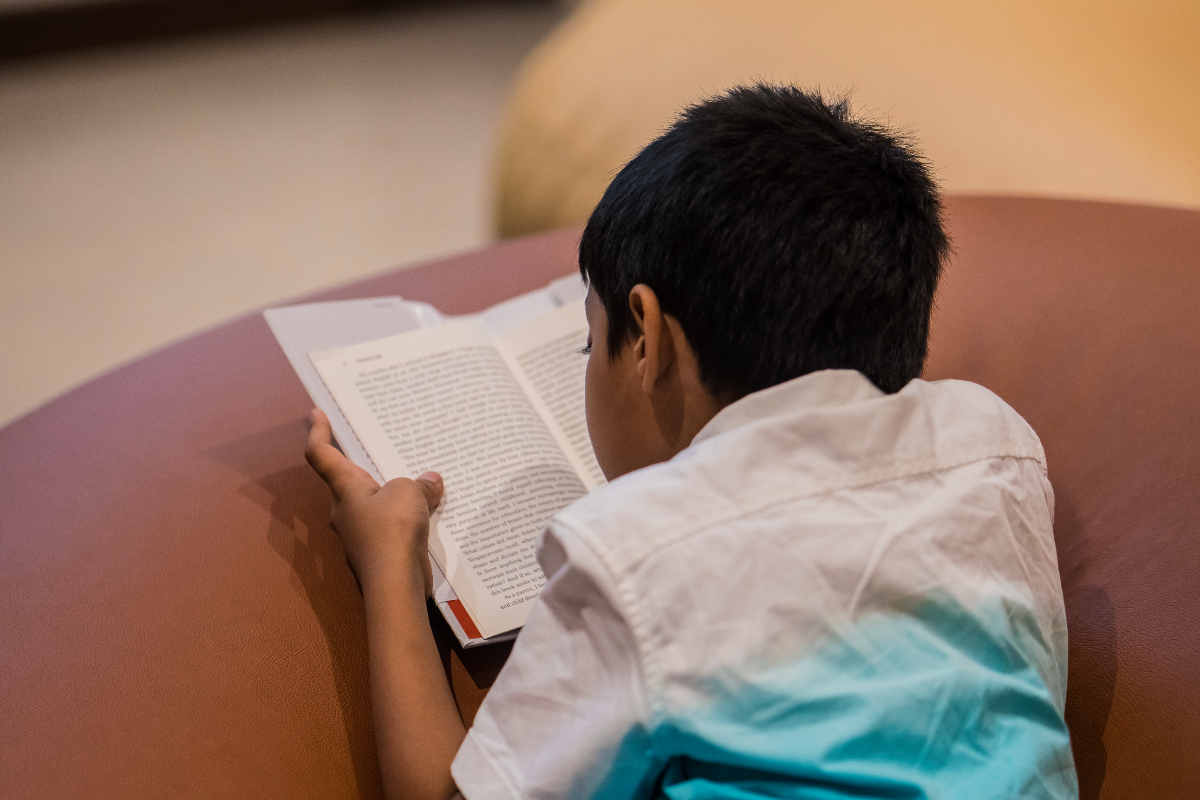 The rear view of a boy engrossed in focused reading.