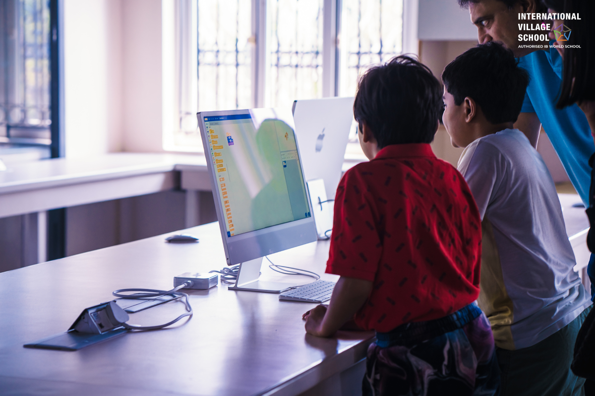 Small boys working on a computer with the assistance of a teacher.