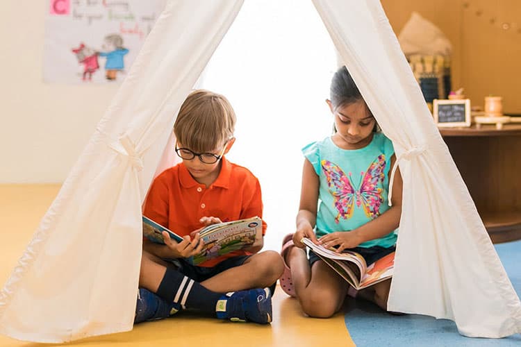 A small boy and a girl reading inside a tipi reading corner in the classroom.